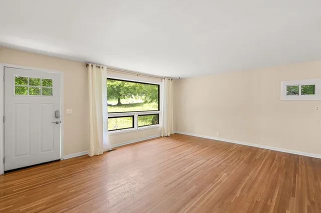 a view of an empty room with wooden floor and a window