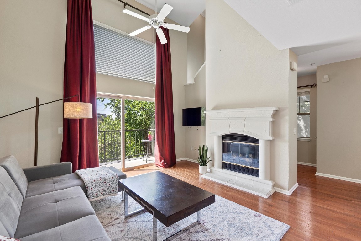 11203 Ranch Road 2222, Unit 207 Austin, TX 78730 - Photo 1 of 1 Living room featuring a towering ceiling, wood finished floors, a ceiling fan, a glass covered fireplace, and plenty of natural light