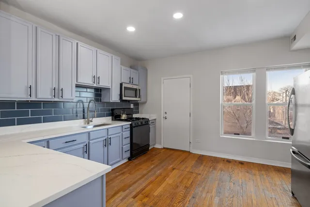 a kitchen with stainless steel appliances granite countertop a stove a sink and white cabinets with wooden floor