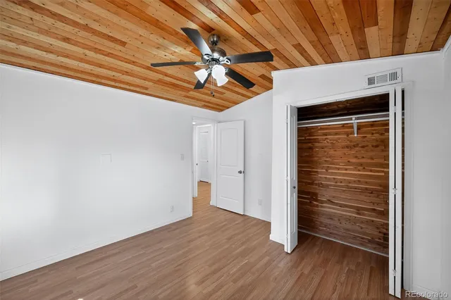 a view of an empty room with wooden floor and a ceiling fan