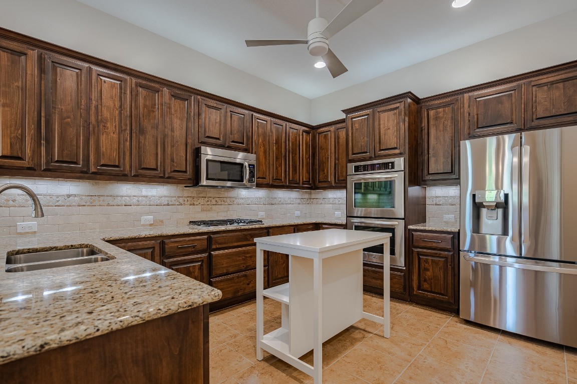 108-2 Rivalto Circle, Unit 5 Lakeway, TX 78734 - Photo 12 of 35 Kitchen featuring dark brown cabinets, appliances with stainless steel finishes, decorative backsplash, light stone counters, and recessed lighting
