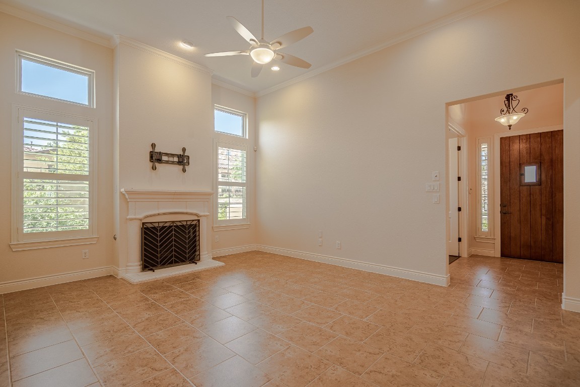 108-2 Rivalto Circle, Unit 5 Lakeway, TX 78734 - Photo 5 of 35 Unfurnished living room featuring ornamental molding, a fireplace with raised hearth, a ceiling fan, and light tile patterned floors