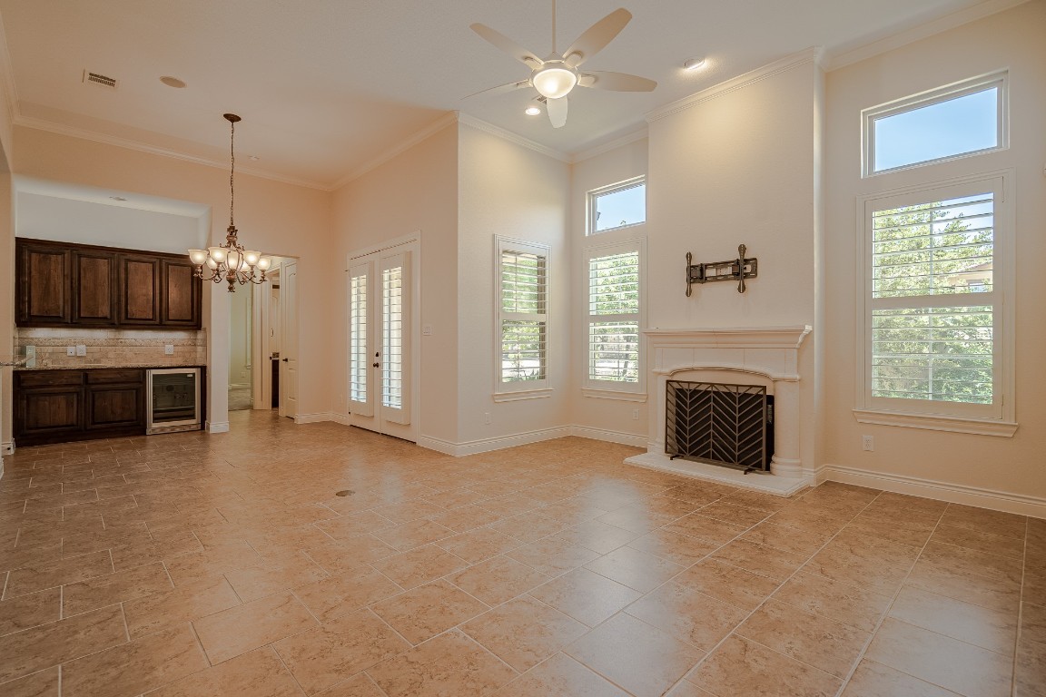 108-2 Rivalto Circle, Unit 5 Lakeway, TX 78734 - Photo 6 of 35 Unfurnished living room featuring healthy amount of natural light, ornamental molding, a fireplace with raised hearth, beverage cooler, and a chandelier
