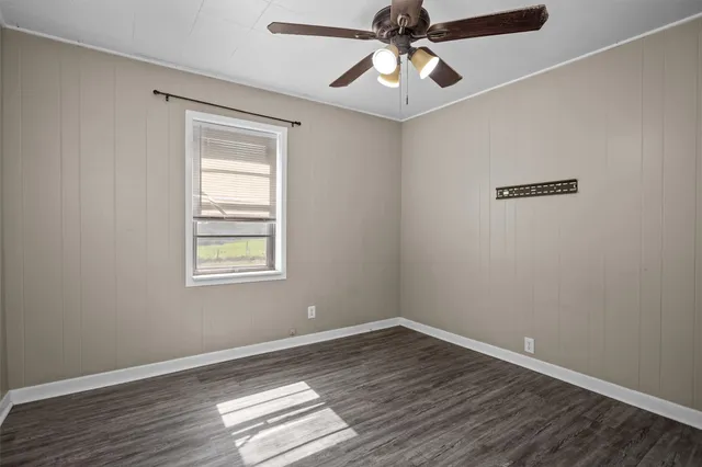 an empty room with wooden floor chandelier fan and windows