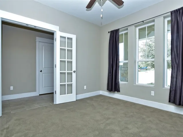 an empty room with chandelier fan and windows
