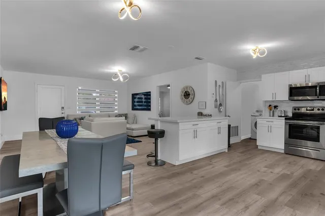 a kitchen with stainless steel appliances kitchen island granite countertop a stove a sink a refrigerator and white cabinets with wooden floor