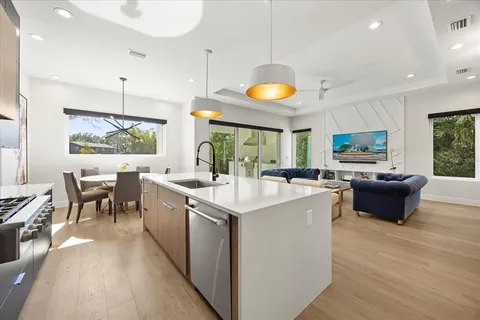 a kitchen with stainless steel appliances granite countertop a stove top oven a sink dishwasher a dining table and chairs with wooden floor