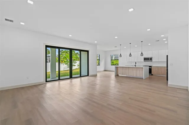 a view of an empty room with wooden floor and a kitchen