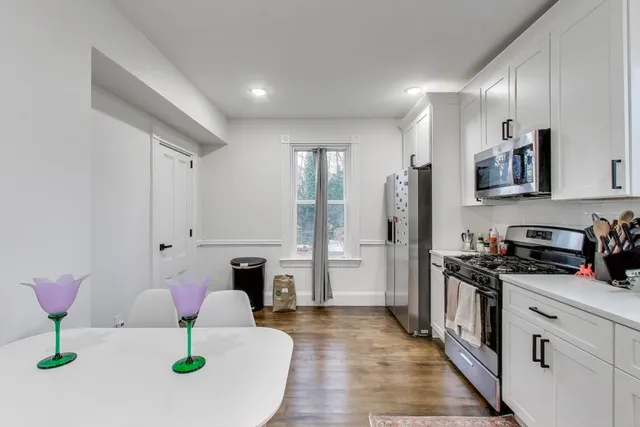 a kitchen with stainless steel appliances kitchen island granite countertop a refrigerator a stove and white cabinets with wooden floor