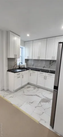 a kitchen with granite countertop a refrigerator a stove a sink and white cabinets