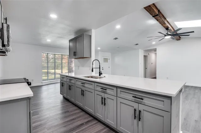 a large kitchen with stainless steel appliances a sink dishwasher a stove and white cabinets with wooden floor