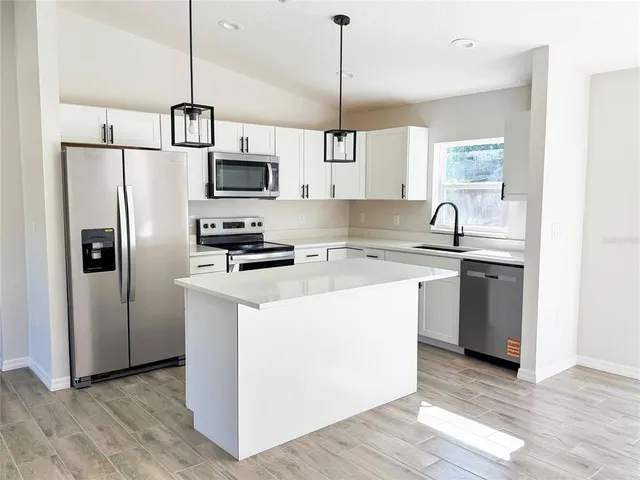 a kitchen with stainless steel appliances granite countertop a refrigerator a sink a stove a microwave and a wooden floor