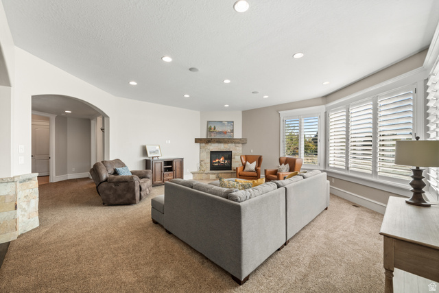 1205 North Elk Rdg Lane, Unit 202 Alpine, UT 84004 - Photo 34 of 88 Spacious living area featuring a stone-clad fireplace with a wood mantel, a series of large windows with white plantation shutters, an arched doorway, recessed lighting, and a neutral carpet