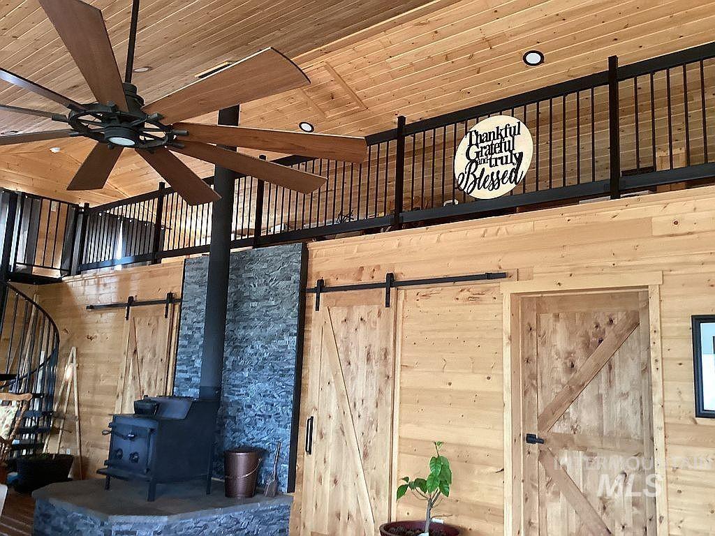 1000 Pardee Road Kamiah, ID 83536 - Photo 13 of 50 Interior space featuring a freestanding wood-burning stove with a stone surround, a black spiral staircase, and wood-finish walls and ceiling