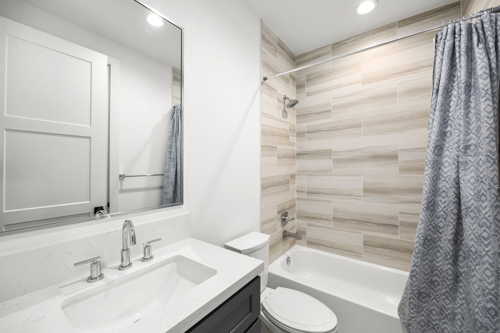 2411 Hazard Street Houston, TX 77019 - Photo 40 of 46 Third-floor bathroom featuring sleek tile work around the tub, a clean white vanity with a modern faucet, and a large mirror providing ample lighting. The neutral tones and contemporary design create a soothing space.
