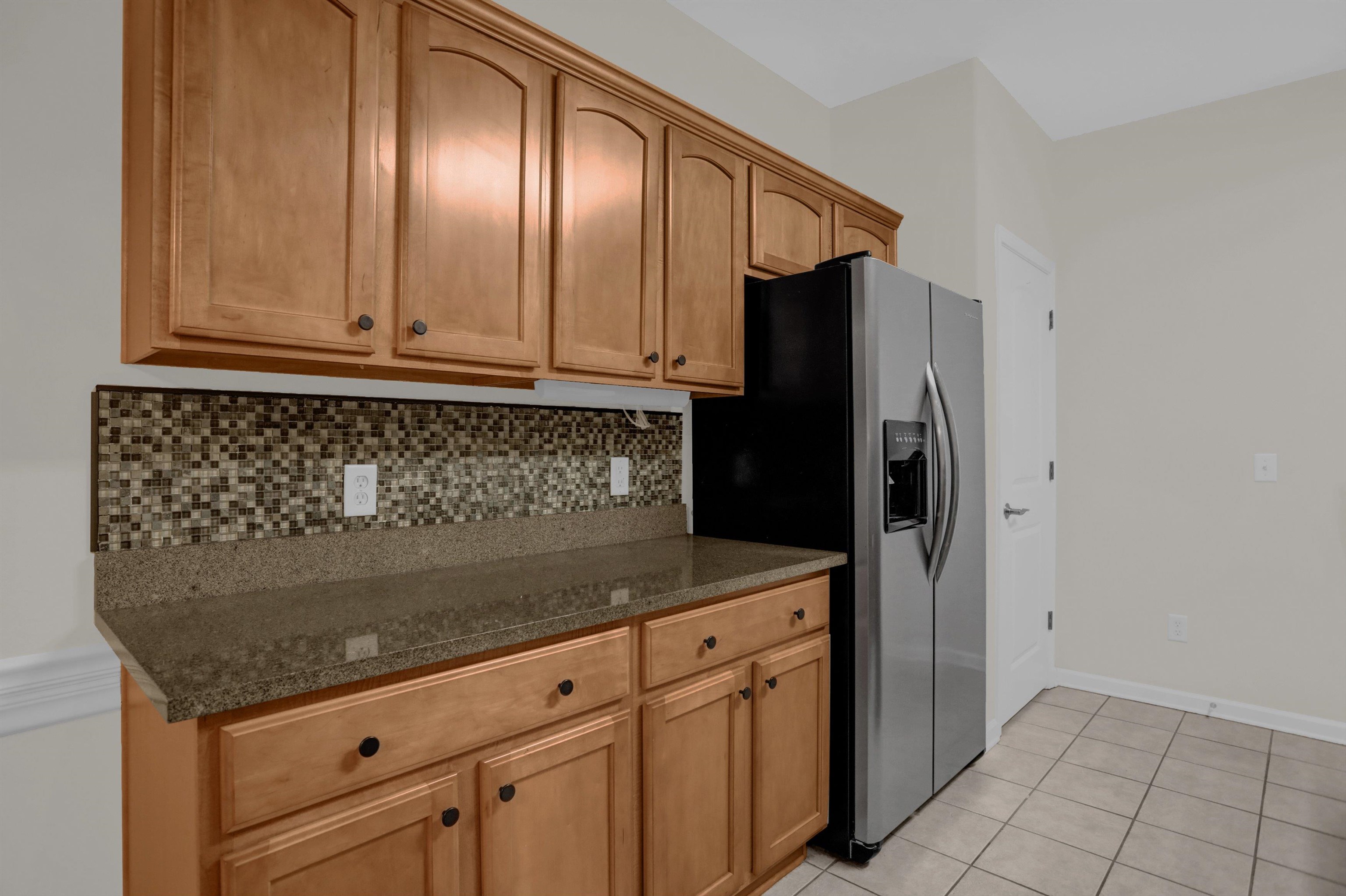 34 Peyton Ridge Drive, Unit 21 Collierville, TN 38017 - Photo 17 of 37 Kitchen featuring wood cabinetry, stone-finish countertops, mosaic tile backsplash, and a stainless steel refrigerator