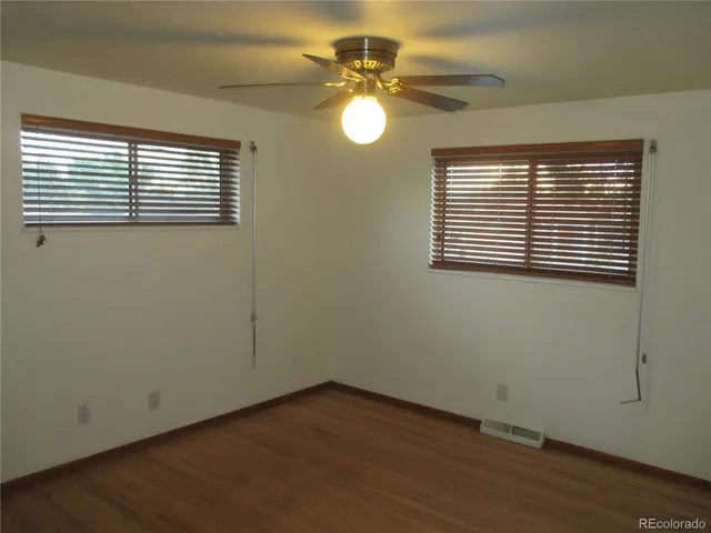 an empty room with wooden floor fan and windows