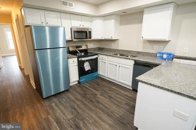 a kitchen with granite countertop a refrigerator stove and sink with wooden floor