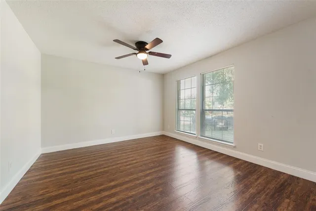 an empty room with wooden floor fan and windows