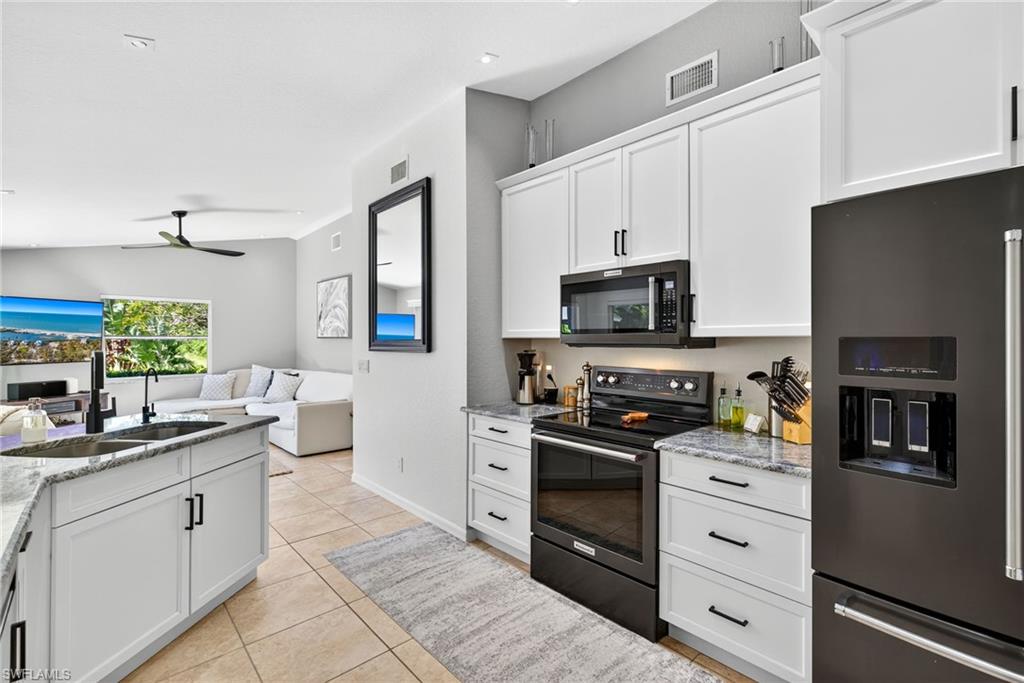 1081 9th Street Southwest Naples, FL 34117 - Photo 11 of 40 Kitchen with refrigerator with ice dispenser, black range with electric stovetop, white cabinets, and light stone counters