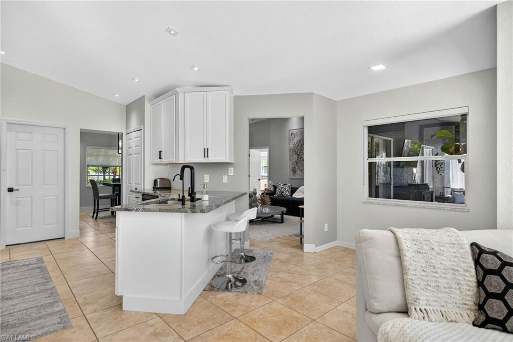 1081 9th Street Southwest Naples, FL 34117 - Photo 10 of 40 Kitchen featuring dark stone counters, white cabinets, a breakfast bar area, light tile patterned floors, and recessed lighting