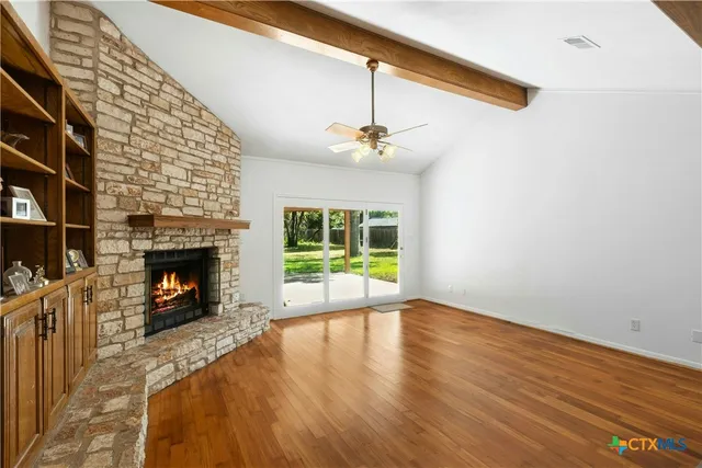 a view of an empty room with wooden floor fireplace and a window