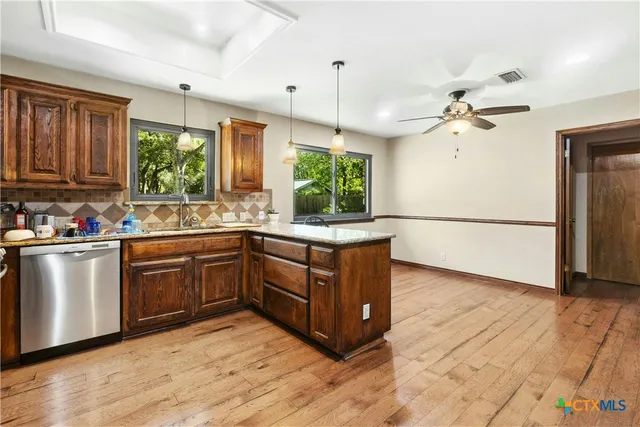 a kitchen with stainless steel appliances granite countertop a refrigerator a sink dishwasher a stove and white countertops with wooden floor