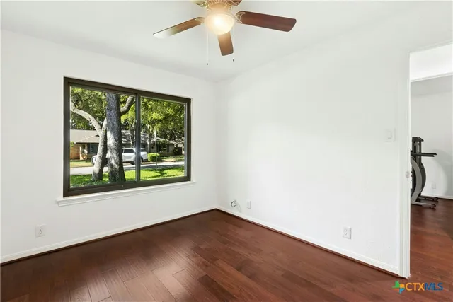 an empty room with wooden floor fan and windows