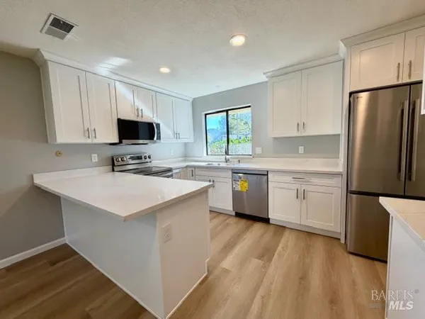 a kitchen with stainless steel appliances a sink a stove a refrigerator cabinets and a window