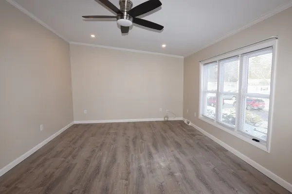 an empty room with wooden floor fan and windows