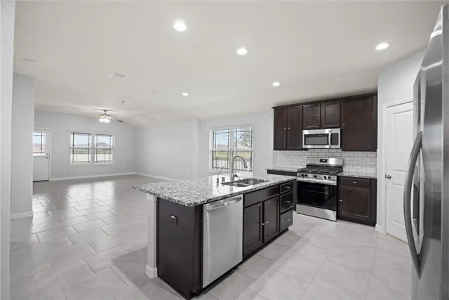 a kitchen with stainless steel appliances granite countertop a stove top oven a sink dishwasher a refrigerator and a dining table with wooden floor