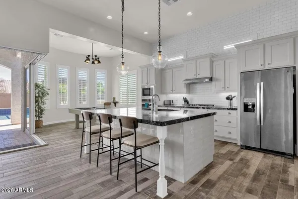 a kitchen with stainless steel appliances granite countertop a sink a stove a refrigerator and chairs