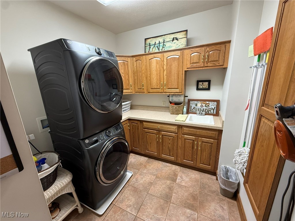 2178 Pleasant Valley Road Northeast New Philadelphia, OH 44663 - Photo 39 of 50 Laundry area featuring stacked washing machine and dryer, cabinet space, and light tile patterned flooring