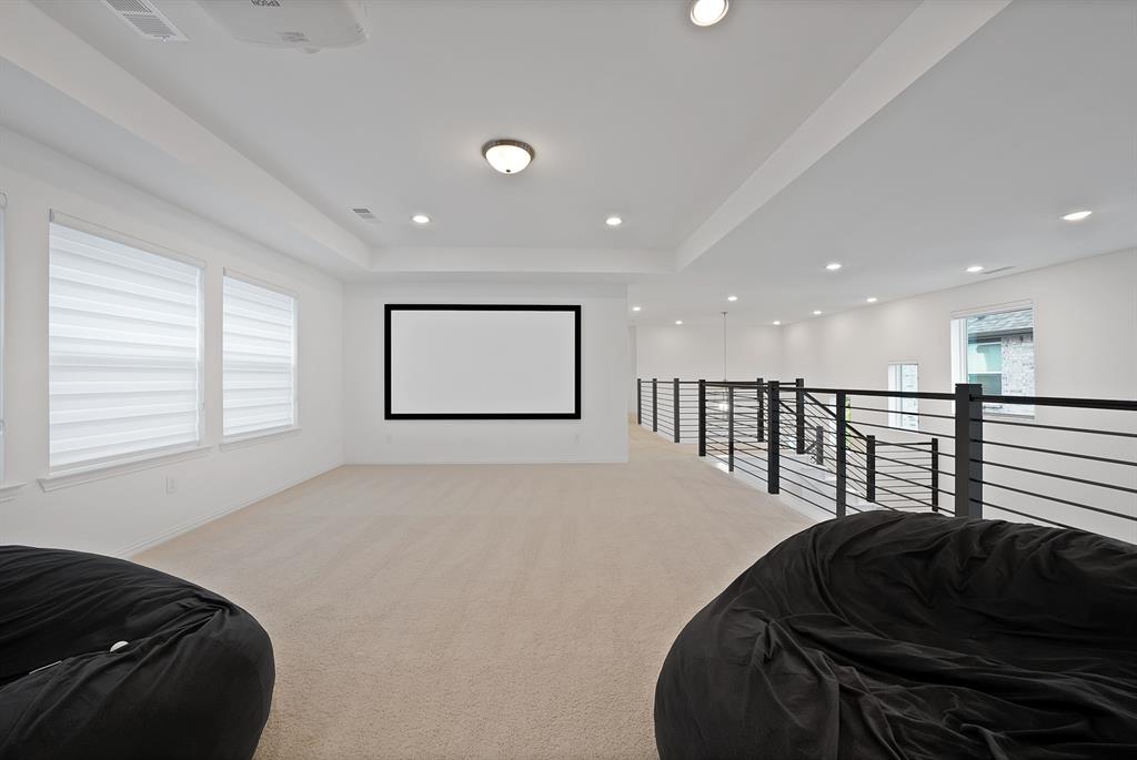 5012 Triadic Lane Prosper, TX 75078 - Photo 27 of 38 Spacious loft area featuring a mounted projector and screen, recessed lighting, neutral carpeting, and a modern black metal railing