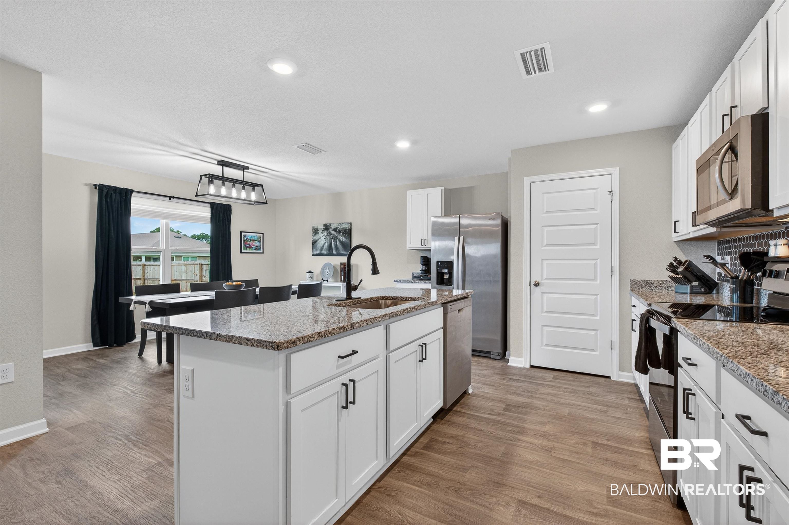 3213 Camino Real Loop Lillian, AL 36549 - Photo 28 of 61 Open-concept kitchen and dining area featuring a central island with a sink, white cabinetry, granite countertops, and wood-finish flooring