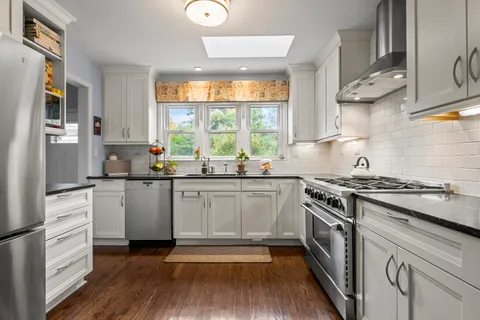 a kitchen with stainless steel appliances a stove a sink and white cabinets with wooden floor