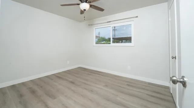 an empty room with wooden floor fan and windows