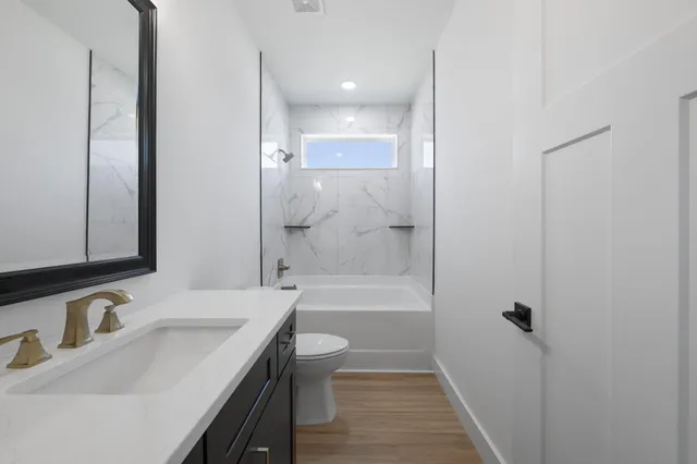 a bathroom with a bathtub shower sink vanity mirror and toilet