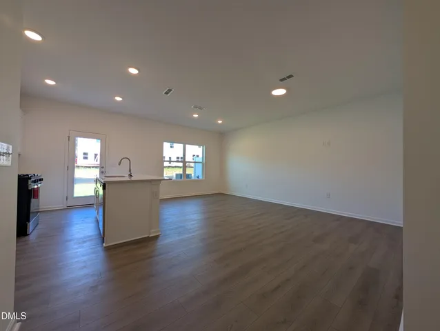 a view of empty room with wooden floor and kitchen view