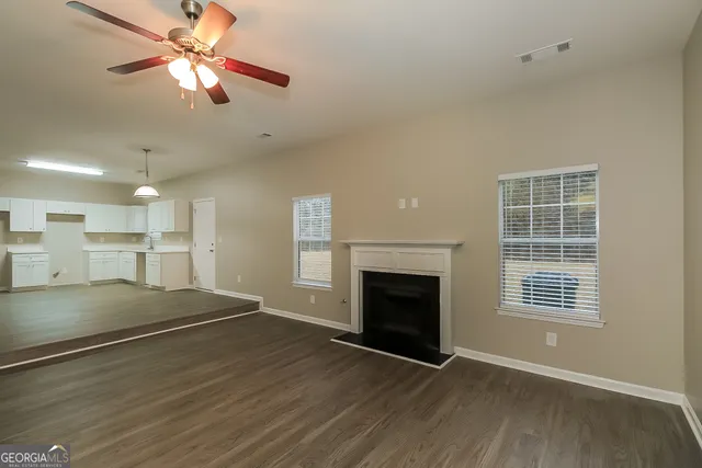 an empty room with wooden floor a ceiling fan a fireplace and windows