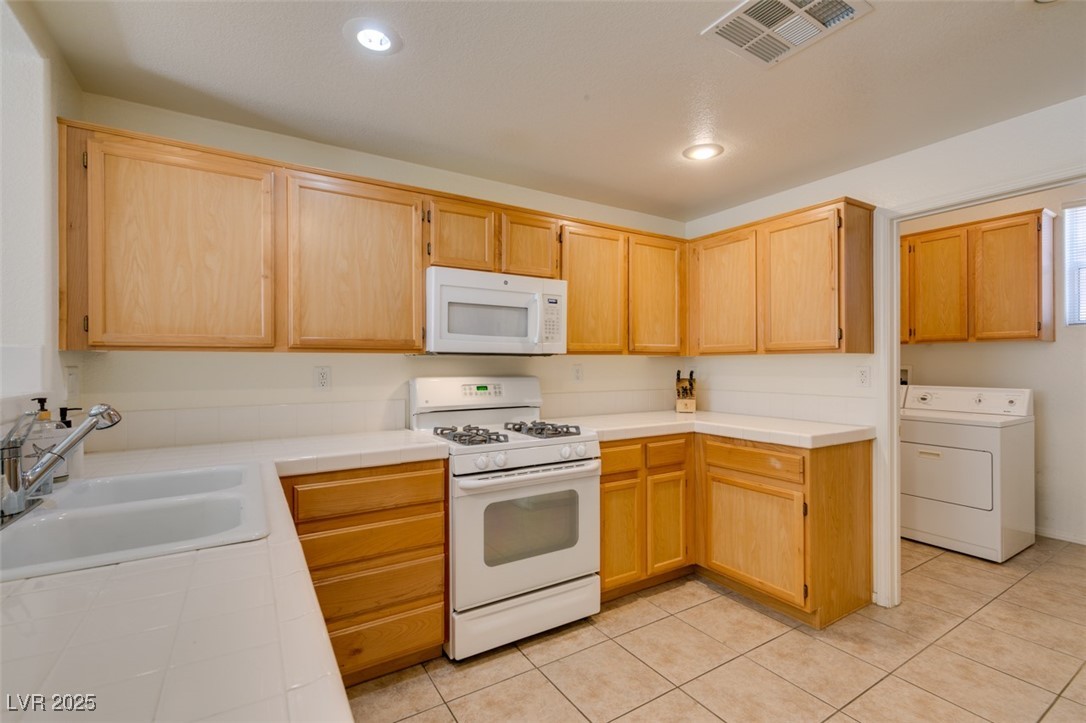 10220 Delray Beach Avenue, Unit 103 Las Vegas, NV 89129 - Photo 24 of 42 Kitchen featuring tile counters, white appliances, a sink, washer / dryer, and visible vents