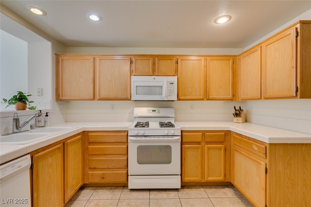 10220 Delray Beach Avenue, Unit 103 Las Vegas, NV 89129 - Photo 25 of 42 Kitchen with light tile patterned floors, a sink, light brown cabinetry, and white appliances