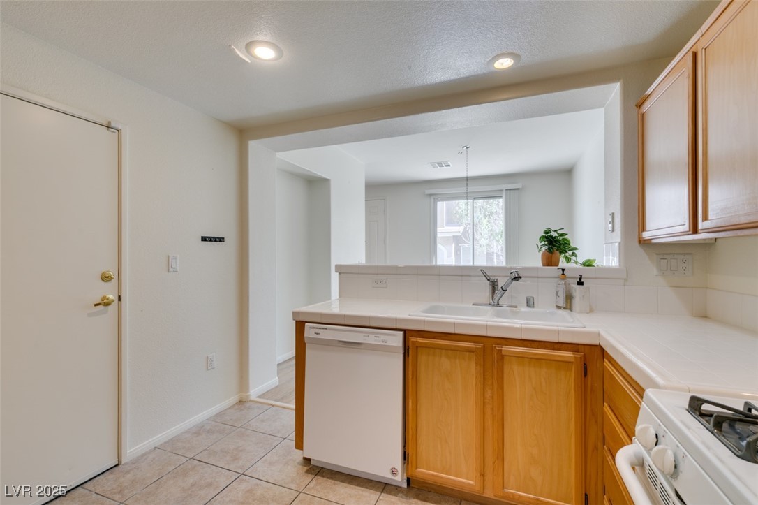 10220 Delray Beach Avenue, Unit 103 Las Vegas, NV 89129 - Photo 27 of 42 Kitchen featuring light tile patterned flooring, tile counters, a peninsula, white appliances, and a sink