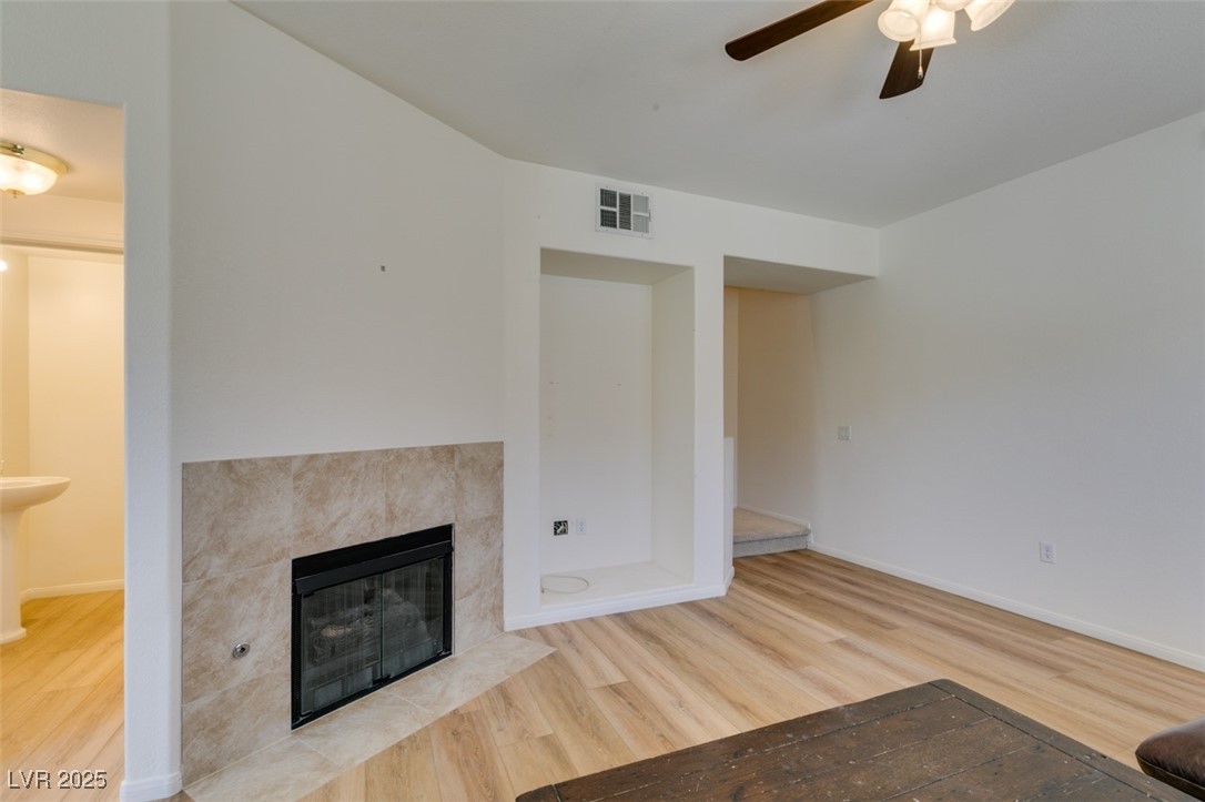 10220 Delray Beach Avenue, Unit 103 Las Vegas, NV 89129 - Photo 8 of 42 Unfurnished living room with visible vents, baseboards, ceiling fan, wood finished floors, and a tiled fireplace