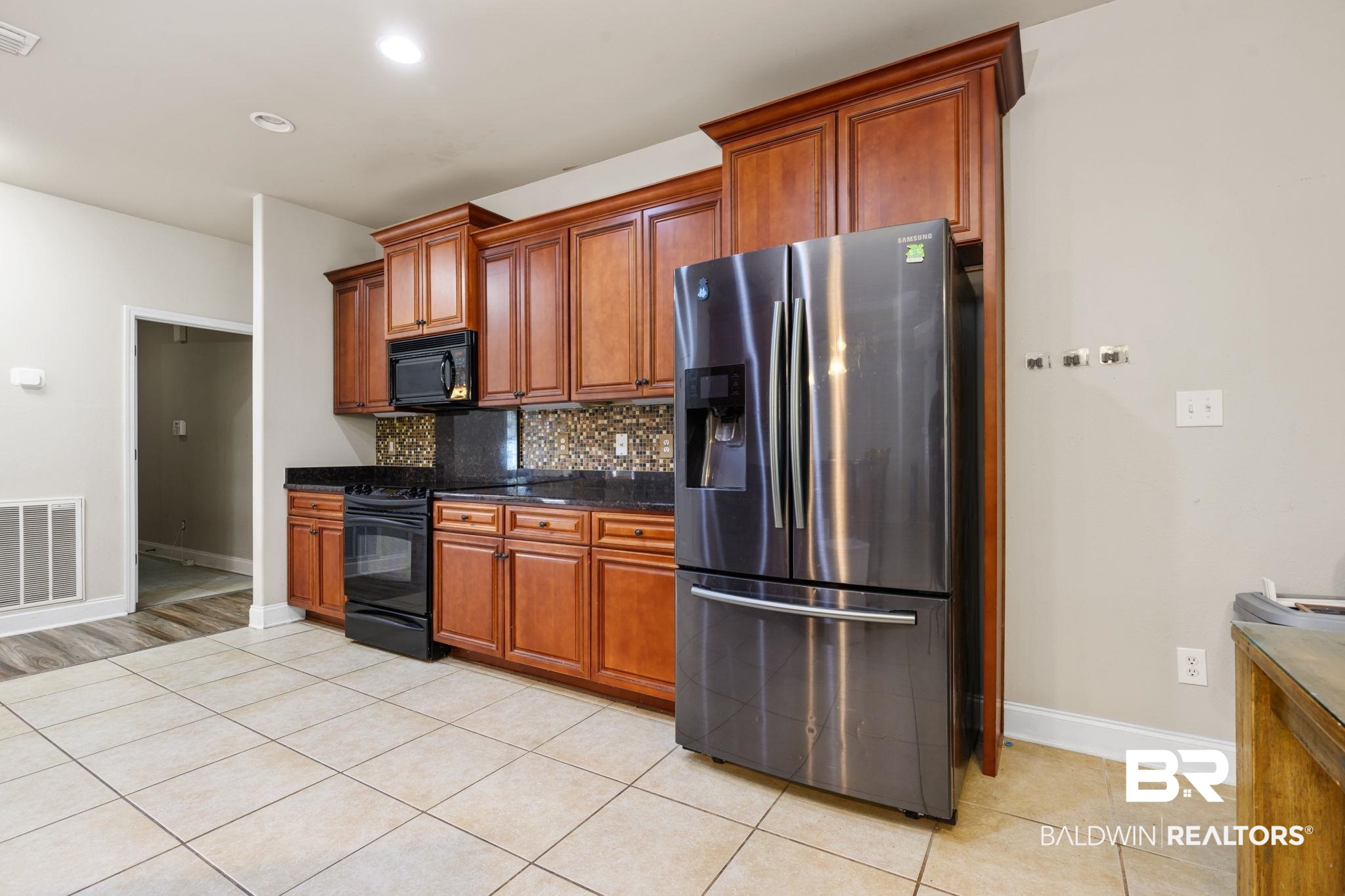7506 Carlson Court Mobile, AL 36619 - Photo 16 of 33 Kitchen with black appliances, brown cabinets, backsplash, light tile patterned floors, and dark stone countertops