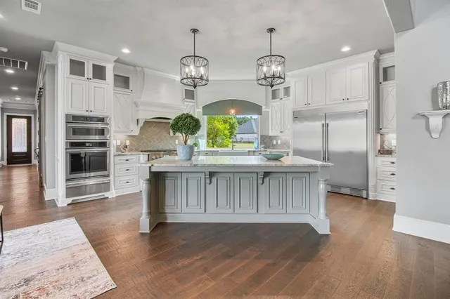 a kitchen with stainless steel appliances granite countertop a refrigerator a sink dishwasher a stove and a dining table with wooden floor