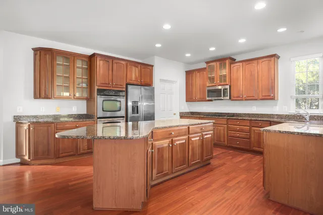 a kitchen with stainless steel appliances granite countertop a refrigerator a oven and a sink with wooden cabinets