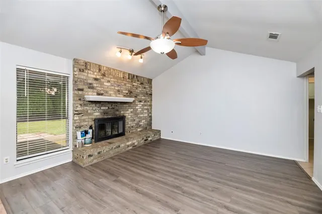 a view of an empty room with wooden floor fireplace and a window