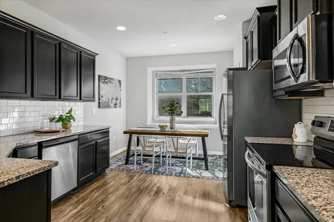 a kitchen with stainless steel appliances granite countertop a stove top oven a sink dishwasher a dining table and chairs with wooden floor