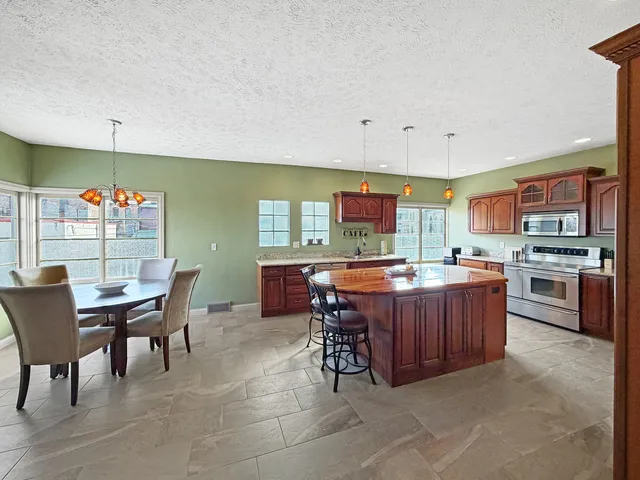 a kitchen with stainless steel appliances granite countertop a stove top oven a sink a dining table and chairs